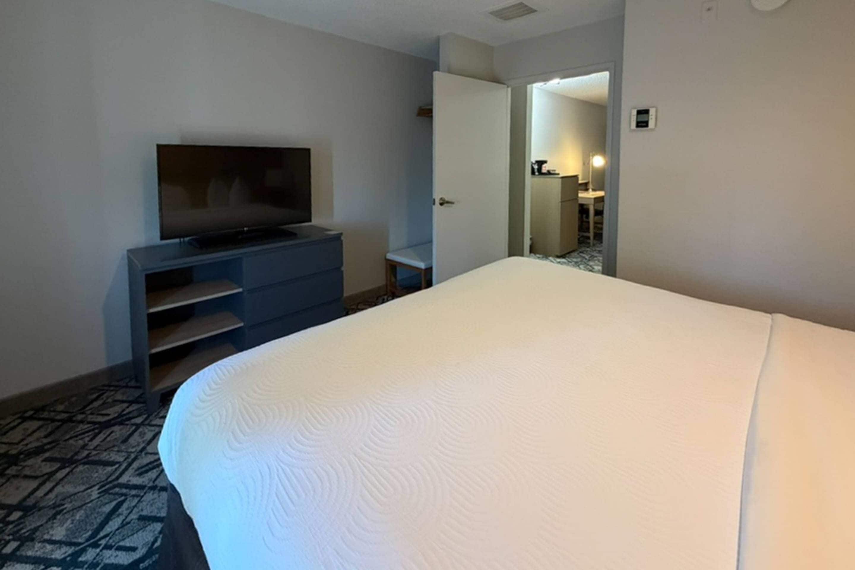 Une chambre d’hôtel avec un grand lit, un téléviseur posé sur un meuble, un bureau et une porte donnant sur une salle de bain.
