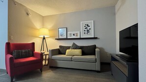 A living room with a red armchair, a grey sofa, a floor lamp, a TV, and framed pictures on the wall.