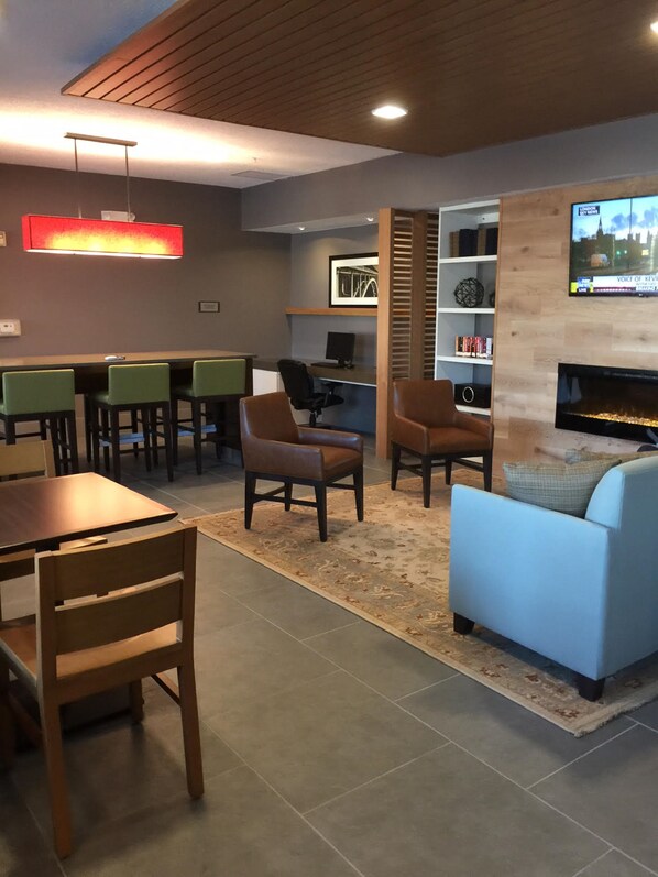 A modern lounge area with a fireplace, seating, and a television displaying a cityscape. - Country Inn & Suites by Radisson, Novi, MI (Novi)