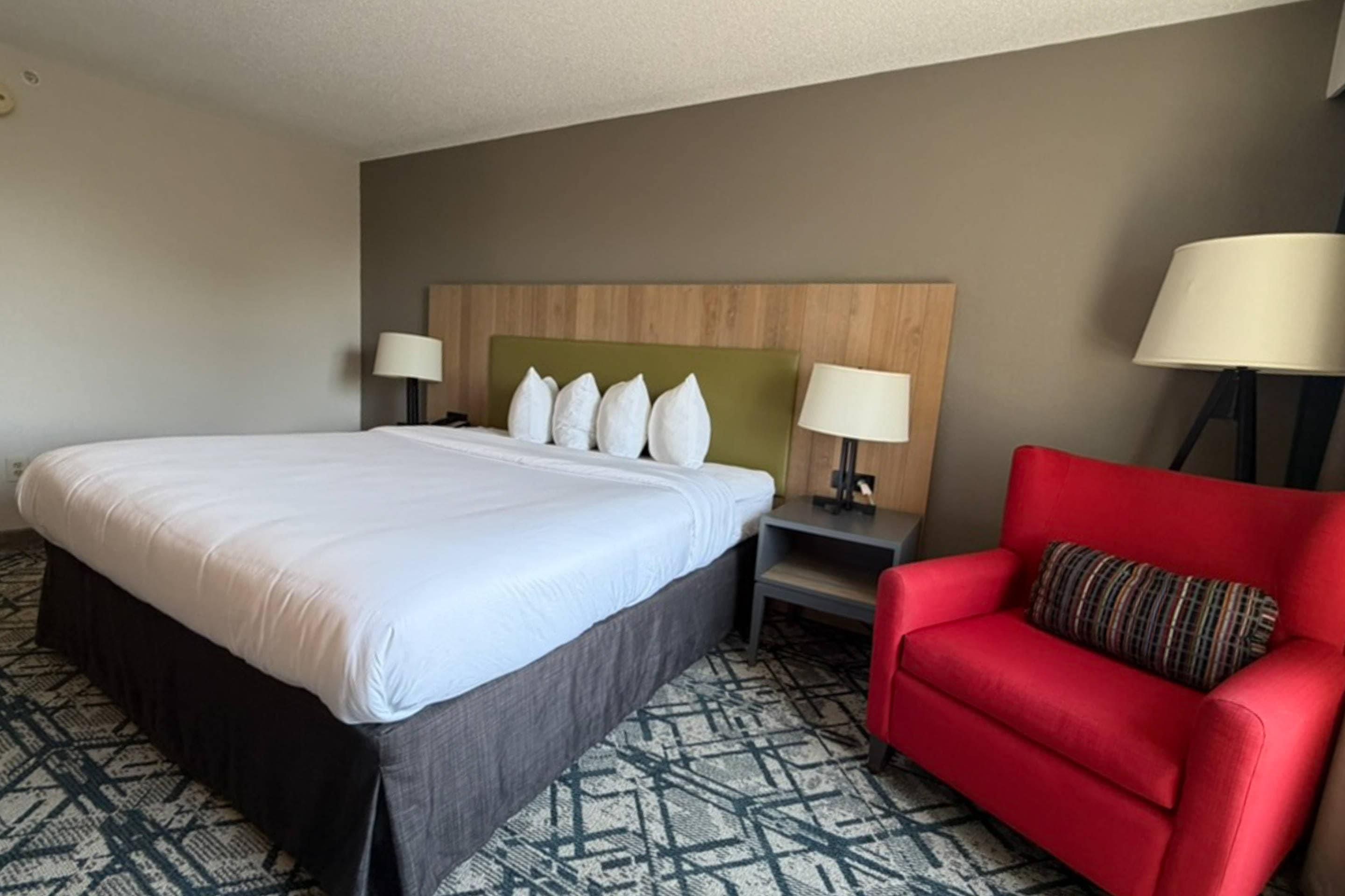 A hotel room with a large bed, two bedside tables with lamps, a red armchair, and a patterned carpet.