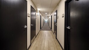 Un largo pasillo de hotel estrecho con puertas oscuras a ambos lados, piso alfombrado e iluminación empotrada en el techo.