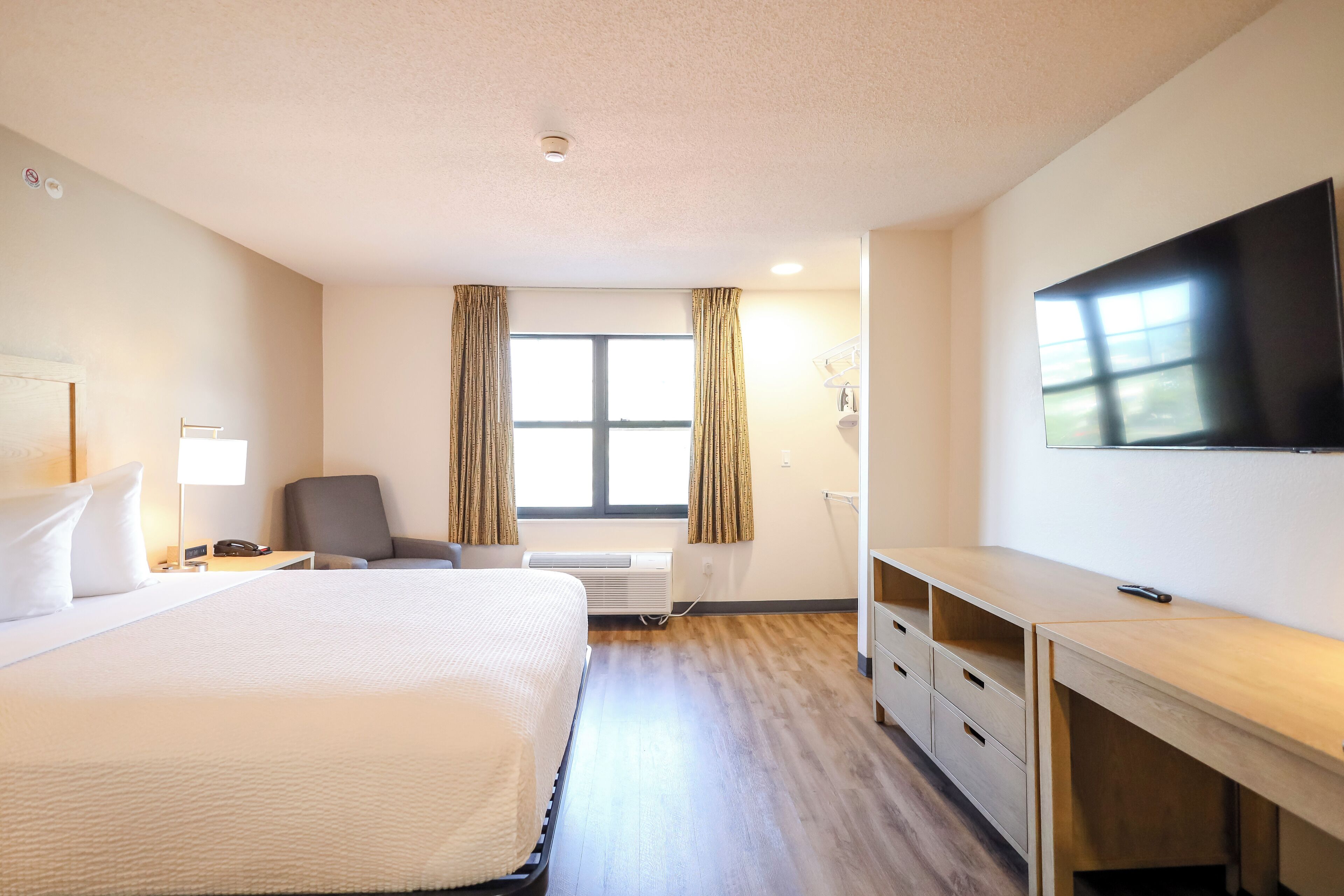 A hotel room with a large bed, a desk, a chair, a TV, and a window with curtains.
