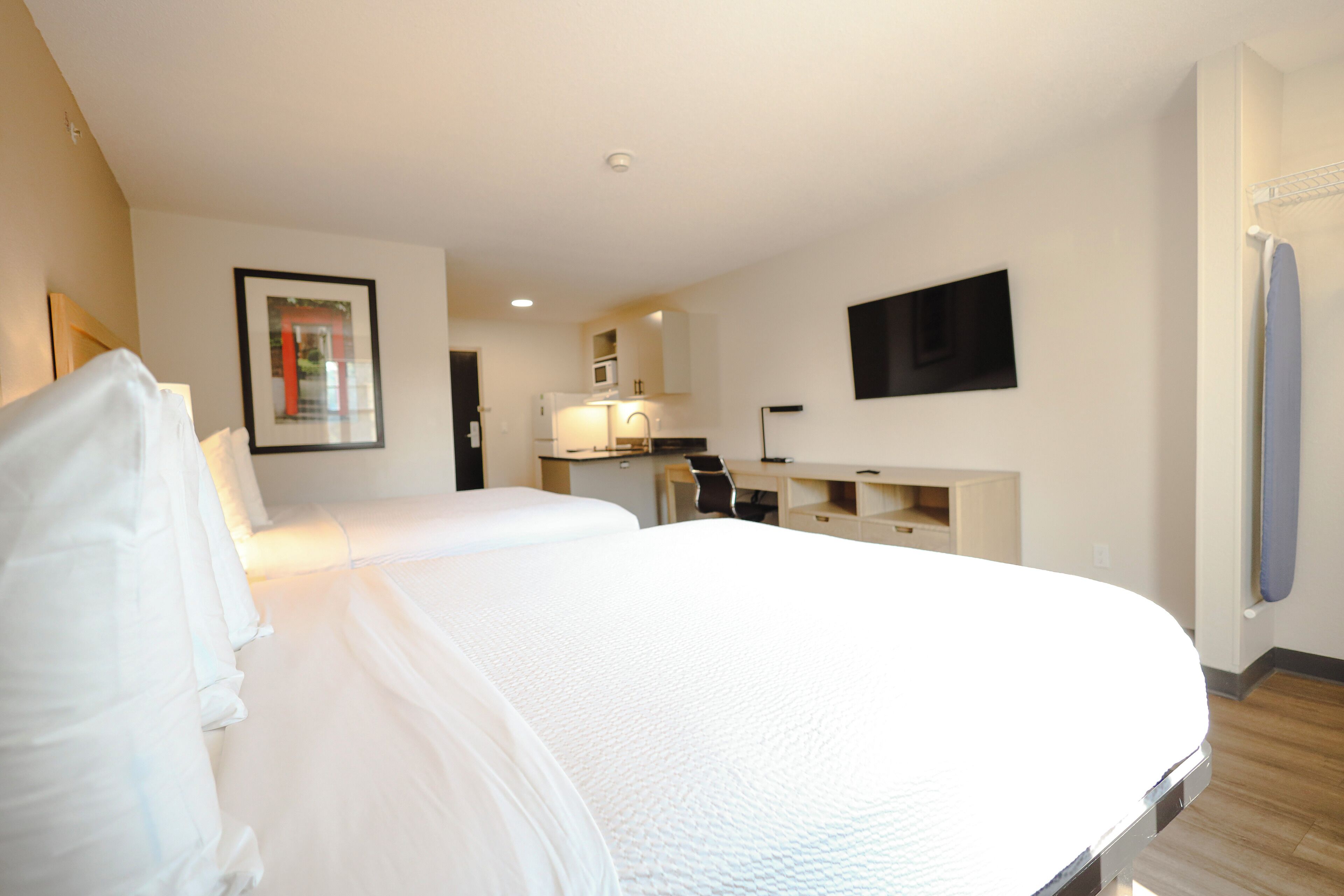 A hotel room with a large bed, a desk, a chair, a flat-screen TV mounted on the wall, and a bathroom with a towel rack.
