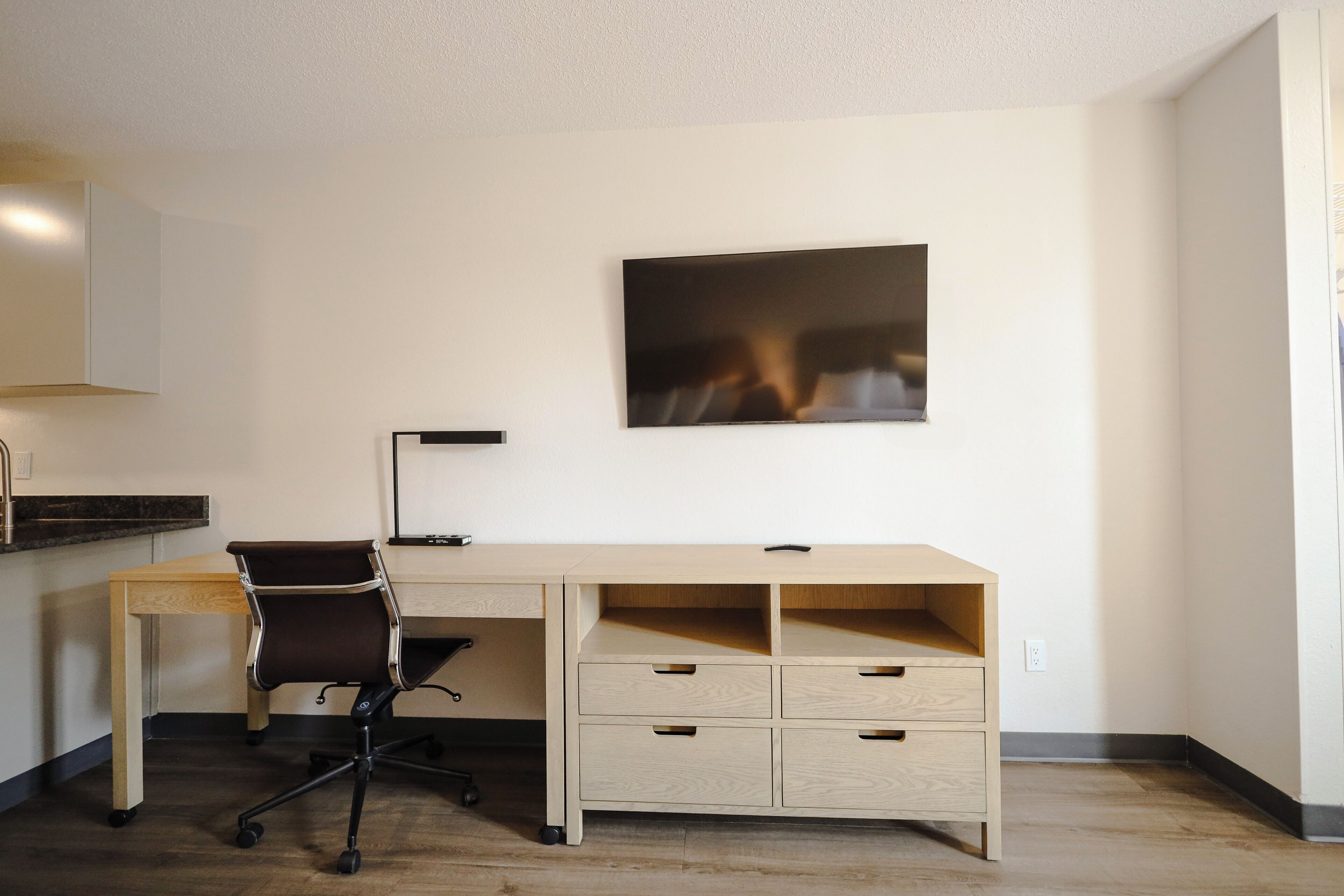 Ein moderner Arbeitsraum mit Schreibtisch, Stuhl und einem gerahmten, abstrakten Kunstwerk an der Wand.