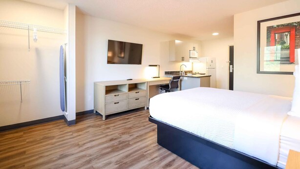 Habitación de hotel con una cama grande, un escritorio con una silla, televisor de pantalla plana, kitchenette y un armario.