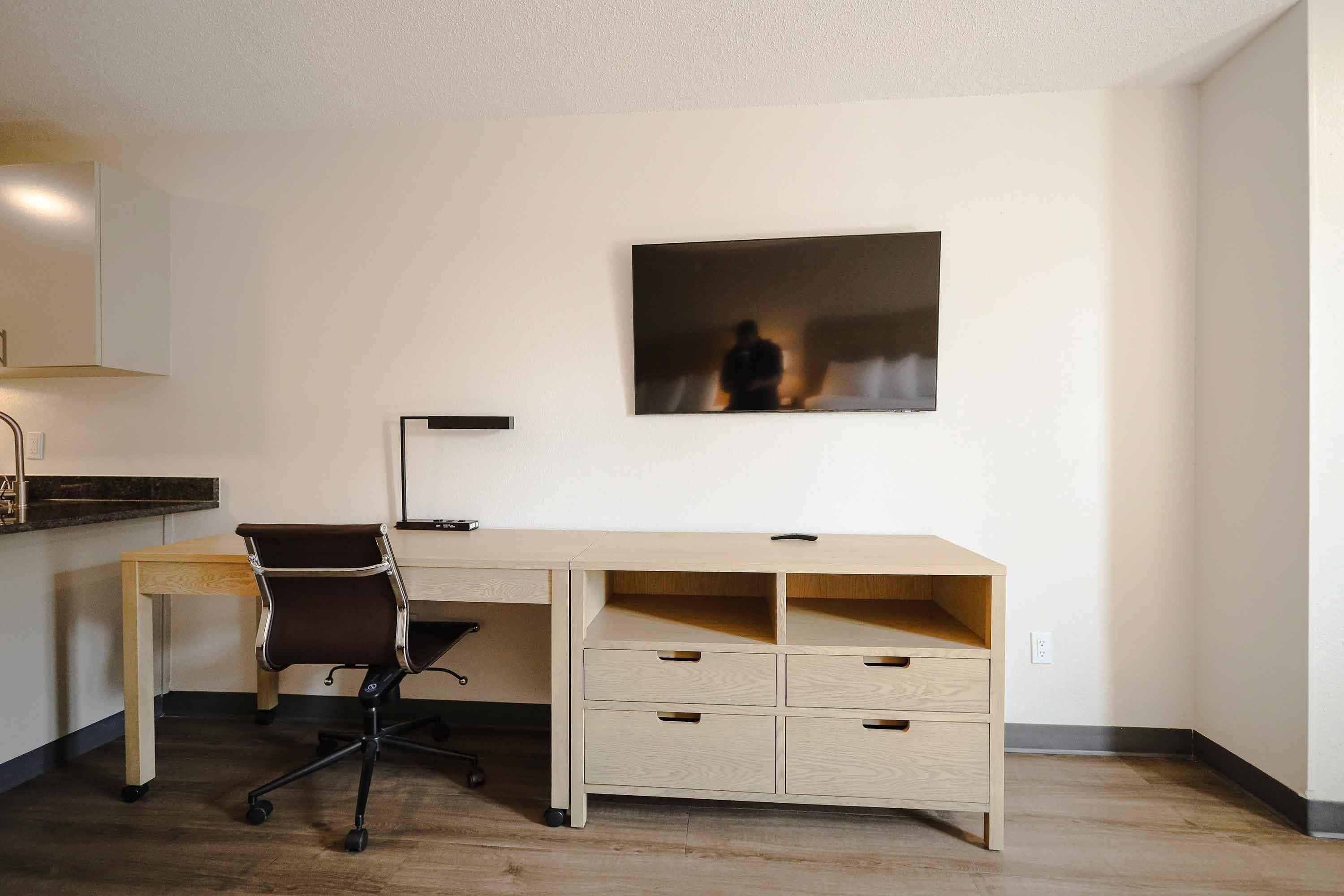 A minimalist office space with a wooden desk, a black office chair, and a single drawer unit.