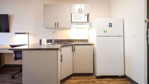 Una cocina compacta con armarios blancos, un microondas y un refrigerador.