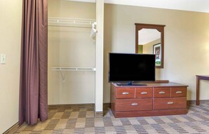 Quarto de hotel com cómoda de madeira, televisão de ecrã plano, espelho e área de chuveiro.