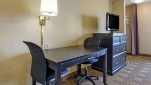 Una habitación de hotel con escritorio, silla, televisor y cómoda.