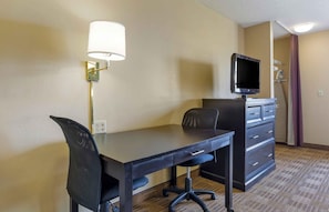 Quarto de hotel com escrivaninha, cadeira, televisão e cómoda.