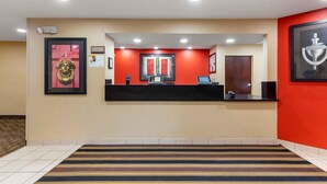 Zona de recepción de hotel con pared roja, mostrador de recepción y un cuadro con un trofeo.