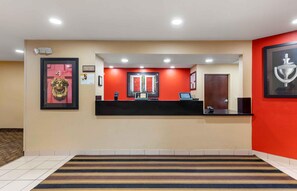 Uma área de recepção de hotel com uma parede vermelha, um balcão de recepção e um quadro emoldurado com uma taça.