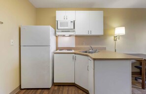A compact kitchen with white cabinets, a microwave, a refrigerator, a sink, and a small island with a chair. - Extended Stay America Suites Austin Southwest (Austin)