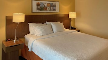 A neatly made bed with white linens, two bedside lamps, a clock, and a framed artwork above the bed.