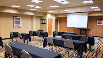 A conference room with tables and chairs, a projector screen, and framed artwork on the walls.