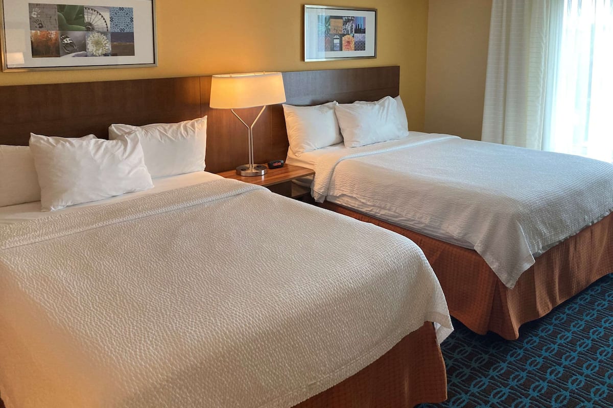A hotel room with two beds, a nightstand, a lamp, and a framed picture on the wall.