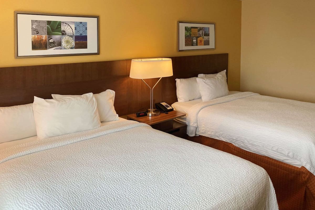 A hotel room with two beds, a nightstand with a lamp, and two framed pictures on the wall.