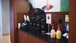 Estação de café com dispensadores da marca e máquina de café, uma placa fixada na parede e uma grande pintura abstrata.