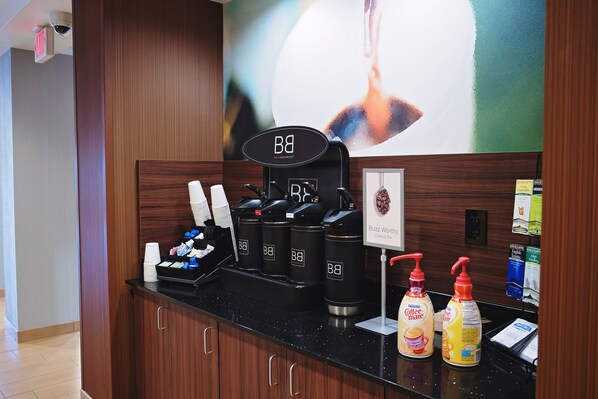 A coffee station with branded dispensers and a coffee machine, a wall-mounted sign, and a large abstract painting.