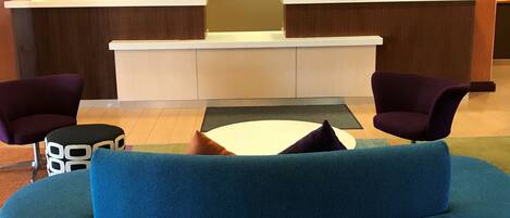 Un área de recepción con un sofá azul, dos sillones morados, una mesita y un mostrador de recepción.