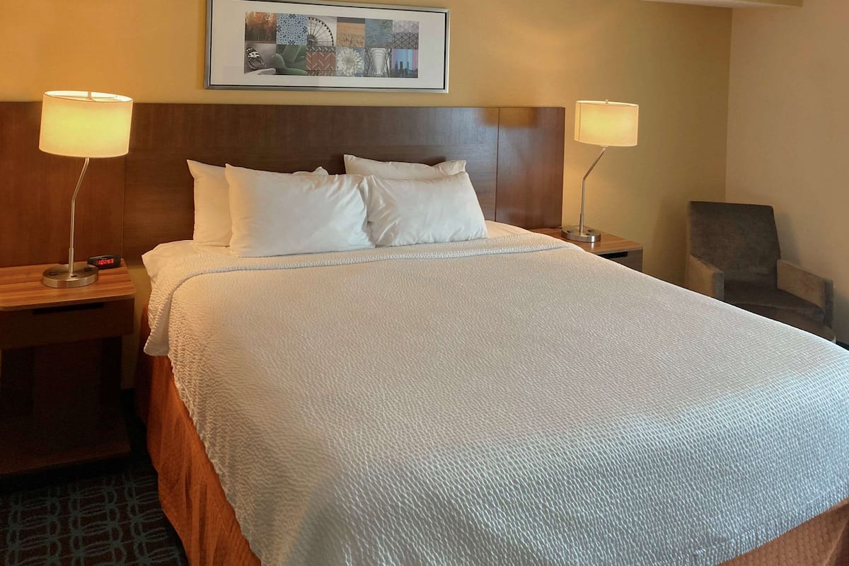 A neatly made bed with white linens, two bedside tables with lamps, a framed picture on the wall, and a chair in the corner.