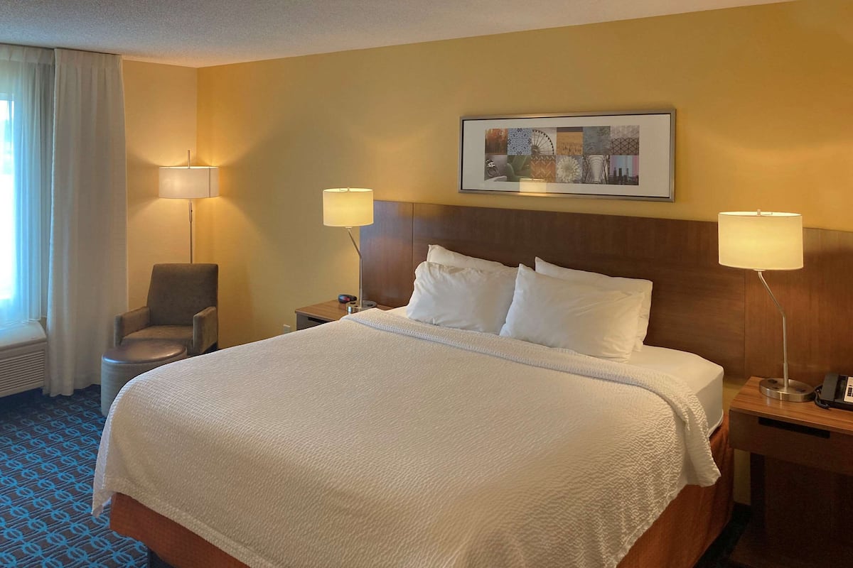 A hotel room with a large bed, two bedside lamps, a chair, a nightstand, and a wall-mounted picture.