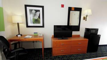 Habitación de hotel con escritorio, una silla, televisión, cómoda, espejo, lámpara y microondas.