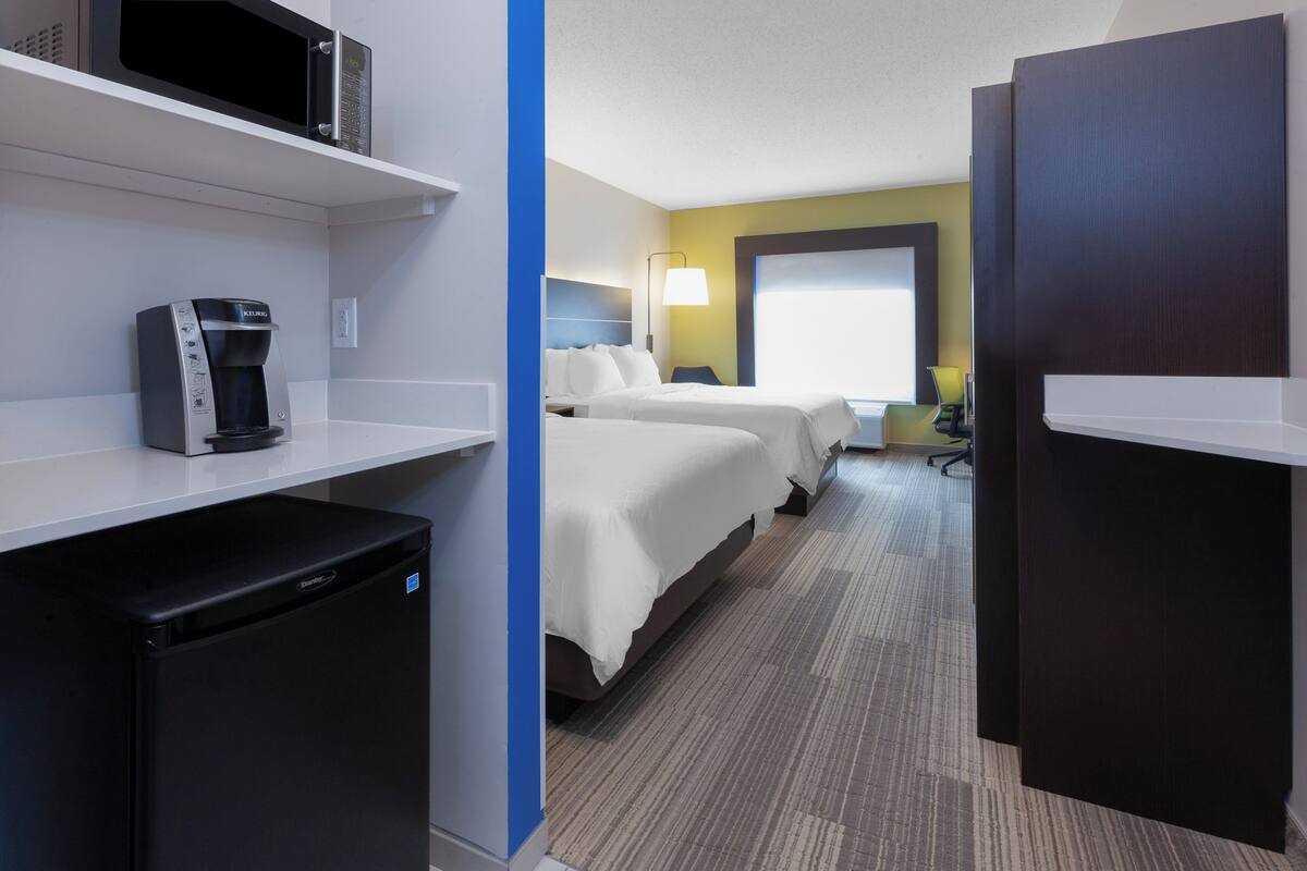 A hotel room with a kitchenette, two beds, a desk, and a window.