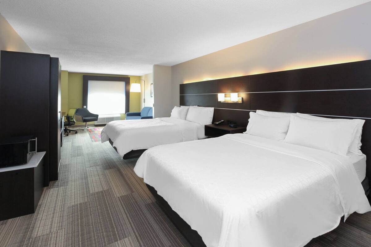 A hotel room with two beds, a desk with a chair, a TV, and a window.