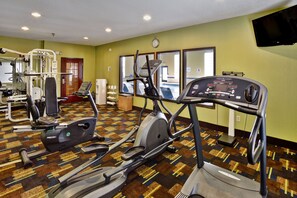 A gym with various exercise equipment, a clock on the wall, and a television mounted above a window. - Holiday Inn Express Hotel & Suites Woodhaven by IHG (Woodhaven)