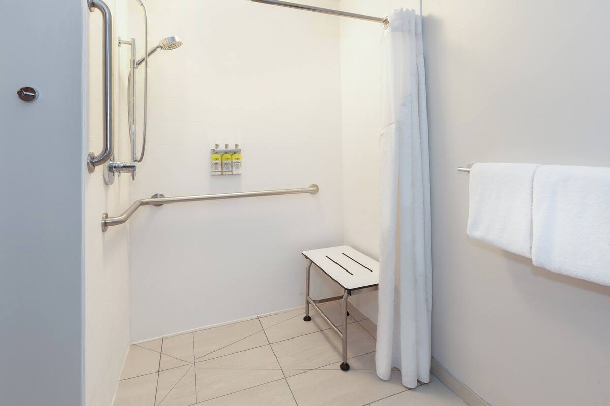 A shower area with grab bars, a white towel rack, and a small table.