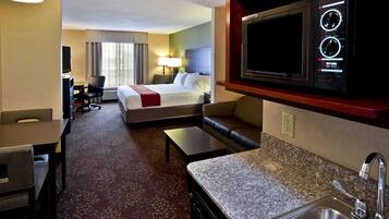 A hotel room with a bed, a desk, a chair, a sofa, a television, a microwave, and a sink.