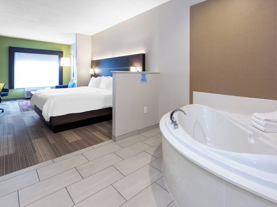 Una habitación de hotel con una cama grande, un baño independiente con bañera y un escritorio con una silla.