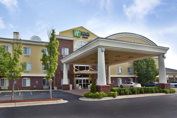 A Holiday Inn Express & Suites with a covered entrance, parking, and a landscaped area with trees and flowers. - Holiday Inn Express Hotel & Suites Woodhaven by IHG (Woodhaven)