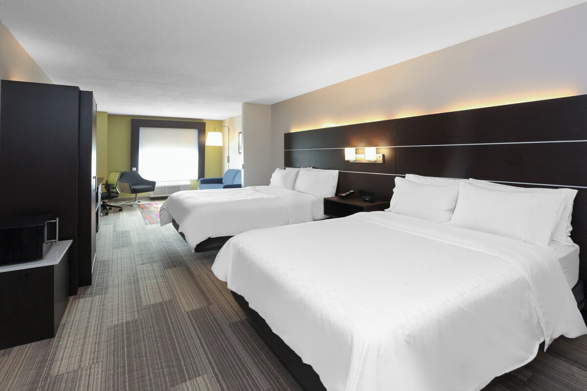 A hotel room with two beds, a desk with a chair, a TV, and a window.
