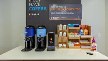 A coffee station with two coffee makers, a sign promoting the IHG Rewards Club, and a display of coffee products and condiments.