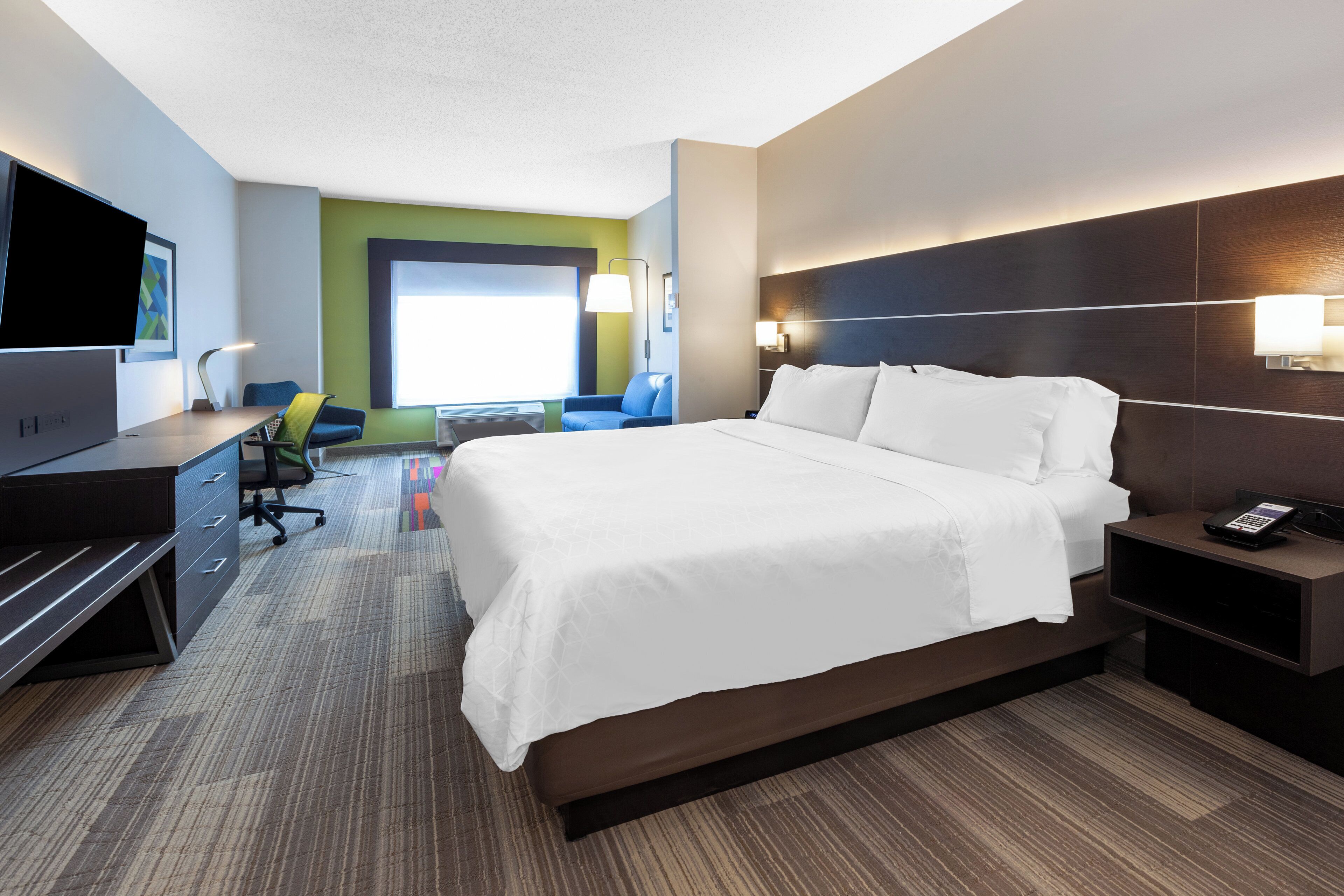 A modern hotel room with a large bed, a desk with a computer, a chair, and a TV.