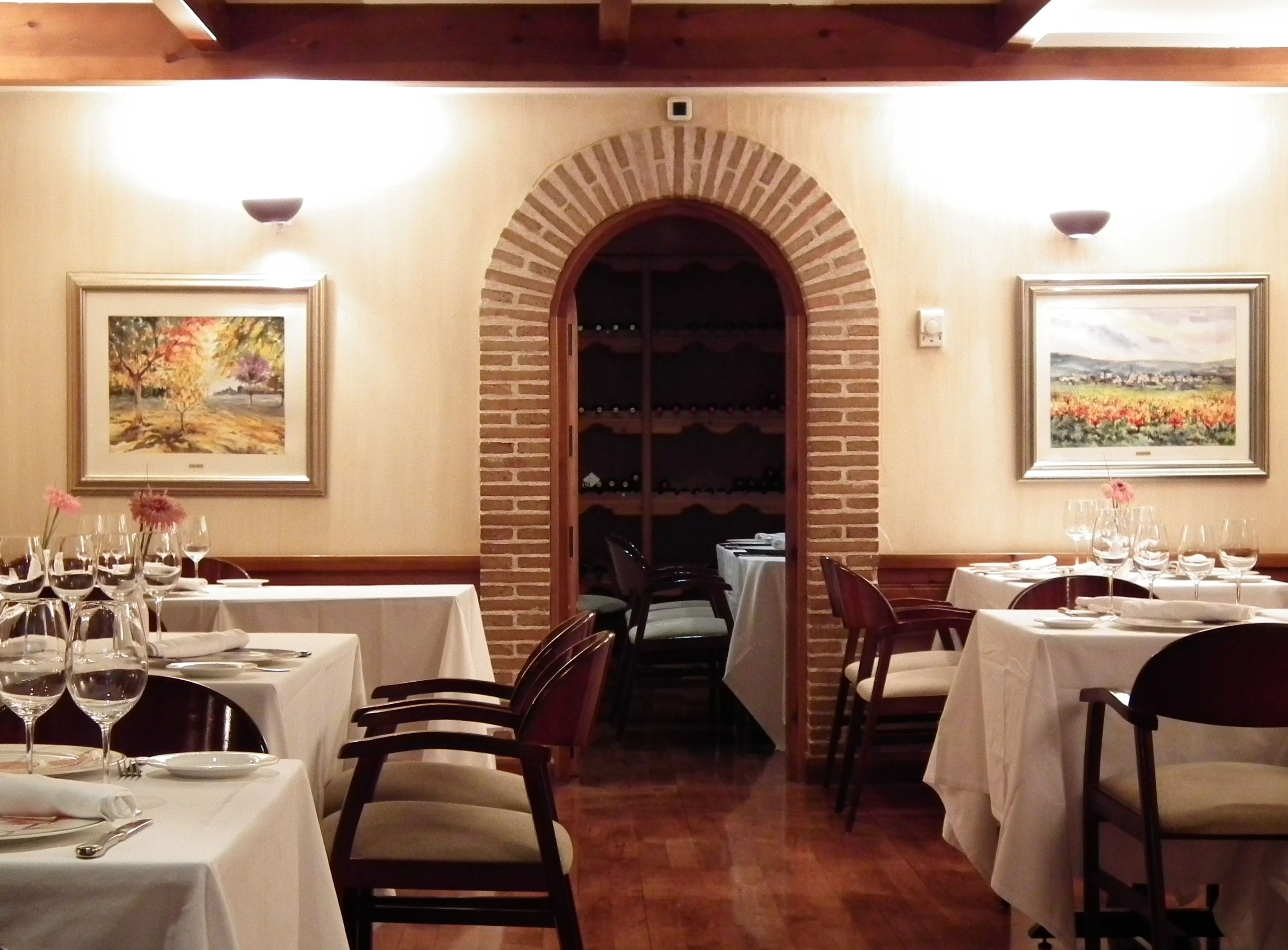 Interior de restaurante con arcos de ladrillo, manteles blancos y copas de vino.