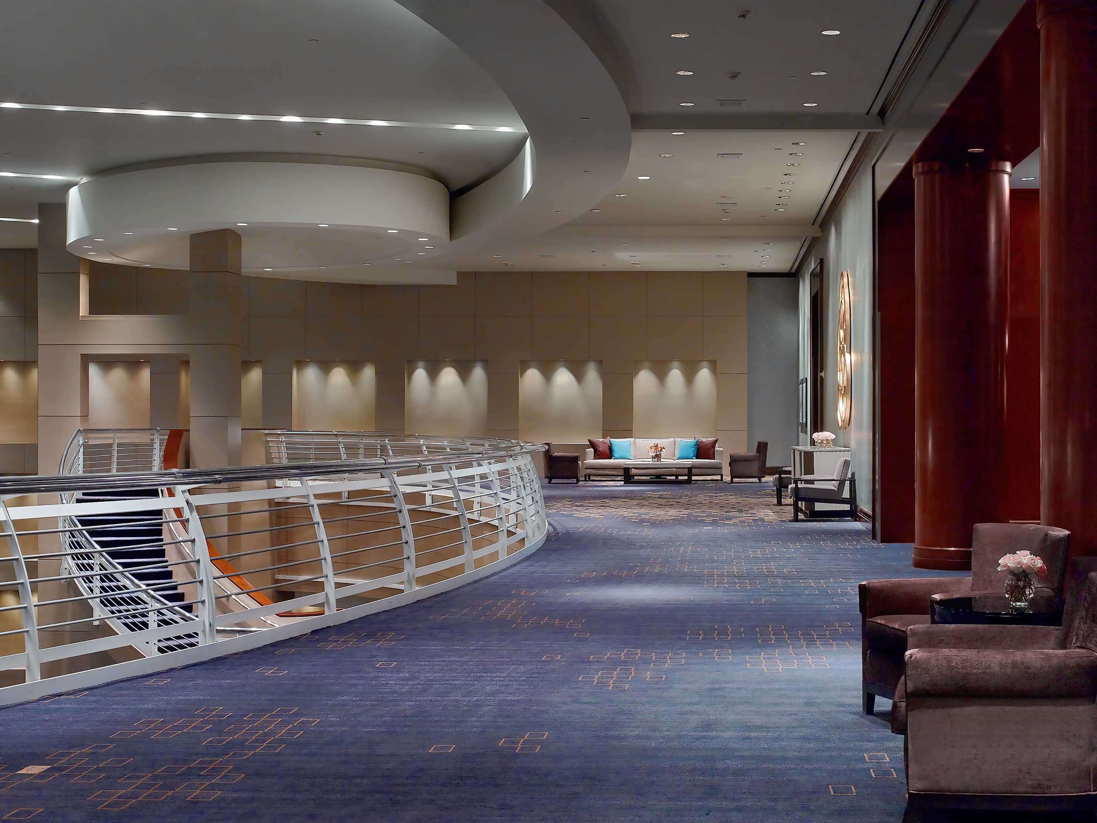 A modern hotel lobby with a curved reception desk, seating area, and a staircase.