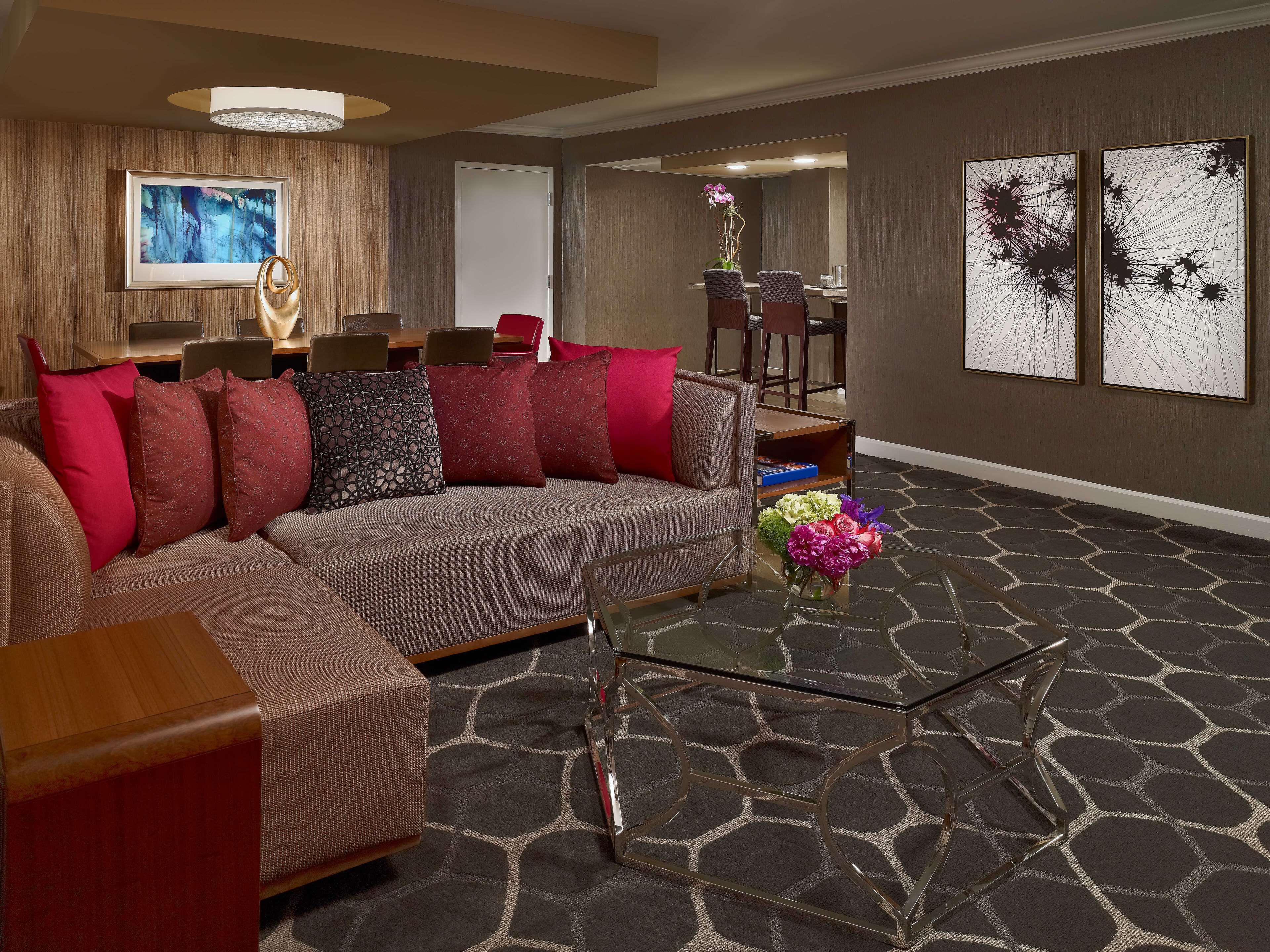 A modern living room with a sectional sofa, a glass coffee table, and a dining area with chairs and a table.