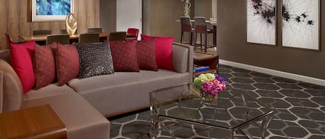 A modern living room with a sectional sofa, a glass coffee table, and a dining area with chairs and a table.
