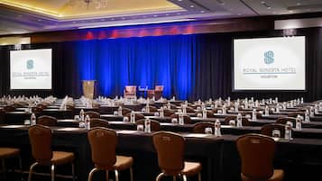 A conference room at the Royal Sonesta Hotel in Houston with rows of tables, chairs, and a stage with a blue curtain backdrop.