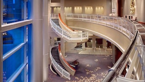 A multi-level hotel interior with a central spiral staircase, a glass elevator, and a patterned carpet.