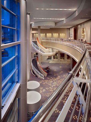 A multi-level hotel interior with a central spiral staircase, a glass elevator, and a patterned carpet. - The Royal Sonesta Houston Galleria (Houston)