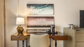 A hotel room with a desk, a lamp, a coffee maker, and a TV.