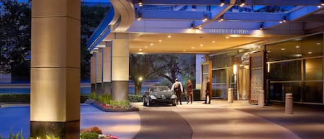 A hotel entrance with a modern design, a covered walkway, and a car parked outside.