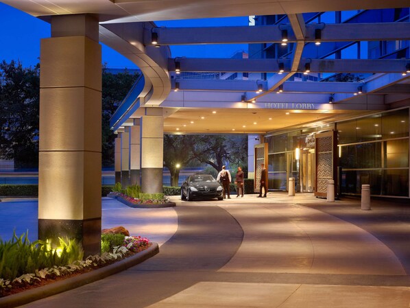 Entrada de hotel con diseño moderno, un vestíbulo cubierto y un coche estacionado afuera.