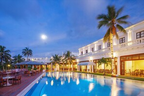 A poolside area with a large pool, palm trees, and outdoor seating.