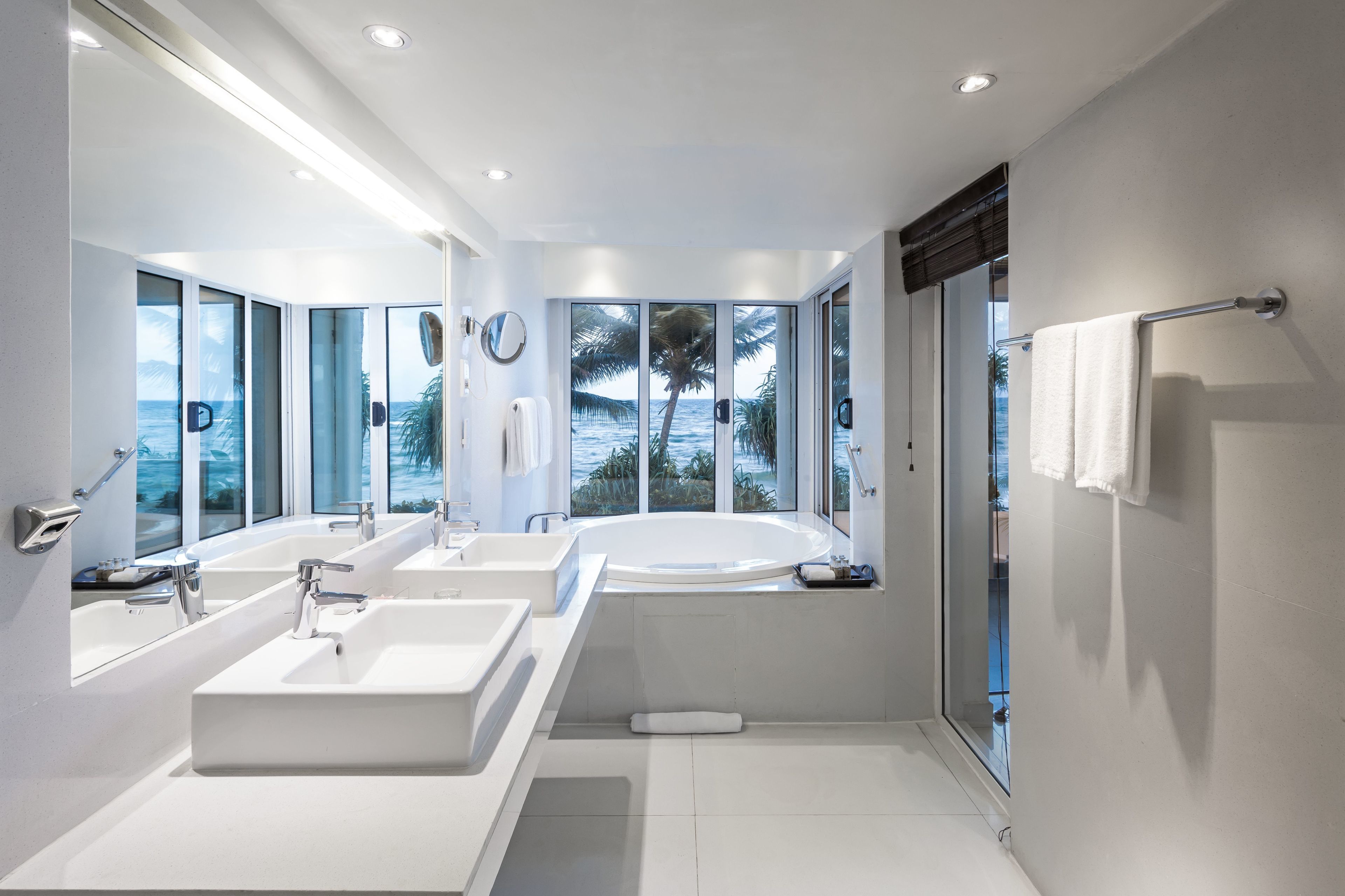 Une salle de bain moderne dotée de deux lavabos, d’une baignoire et de grandes fenêtres offrant une vue sur l’océan.