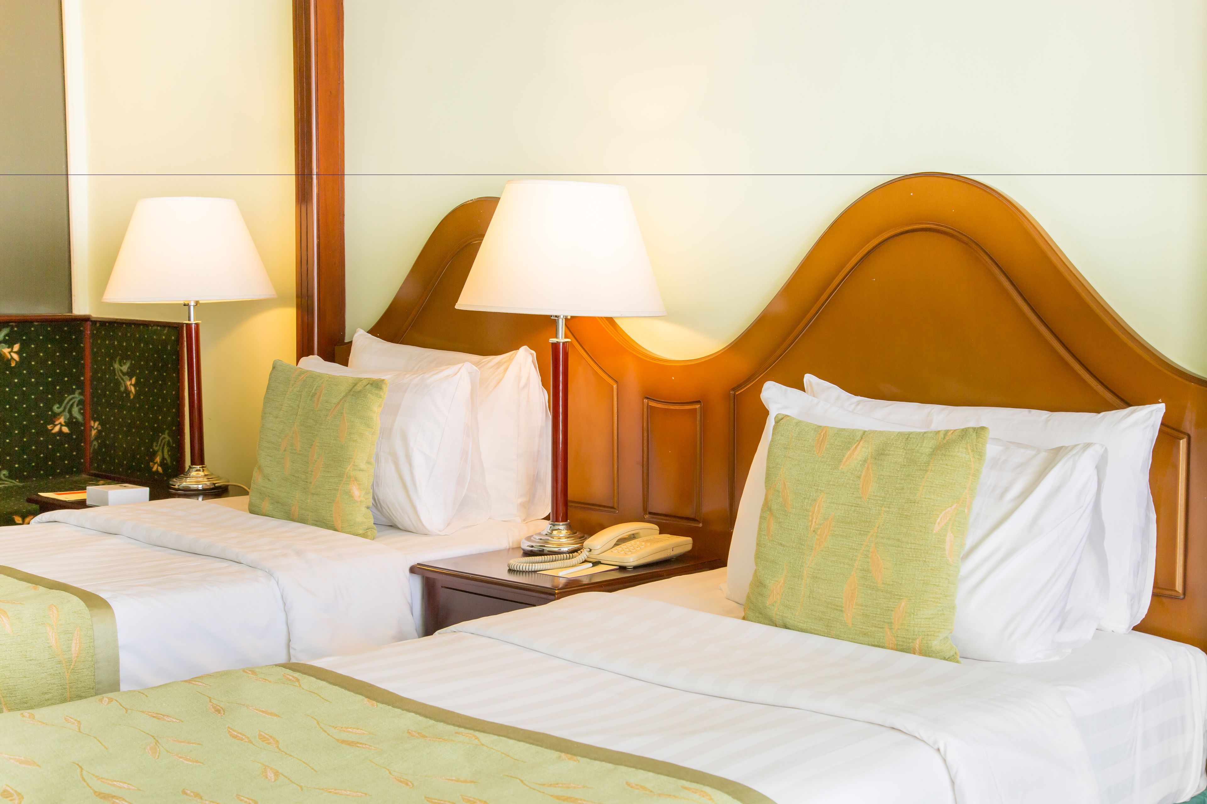 A hotel room with two beds, each with a pillow and a lamp. There is a nightstand with a phone and a lamp between the beds.
